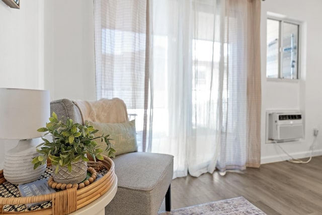 living area with healthy amount of natural light, wood finished floors, and a wall unit AC