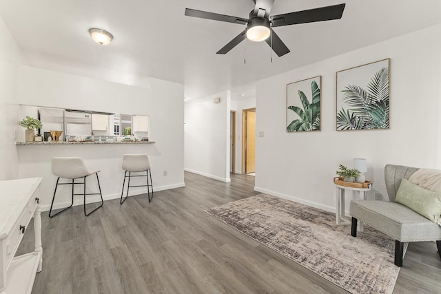 living room with wood finished floors, a ceiling fan, and baseboards