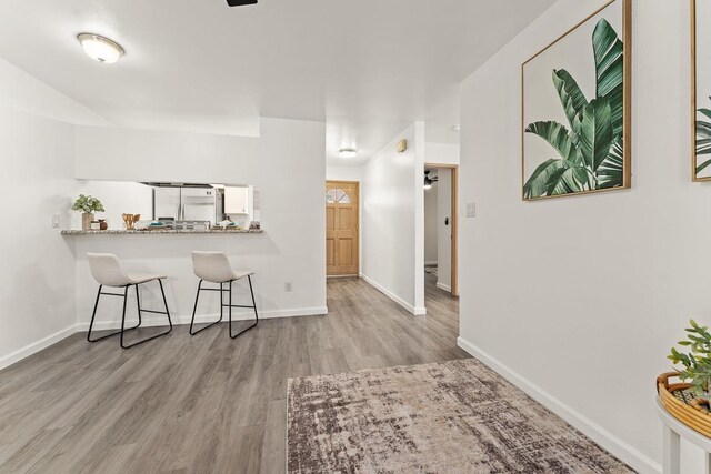 kitchen featuring wood finished floors, stainless steel fridge, a kitchen breakfast bar, and baseboards