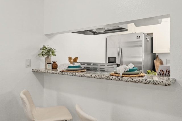 kitchen with stainless steel fridge, white cabinetry, and light stone counters