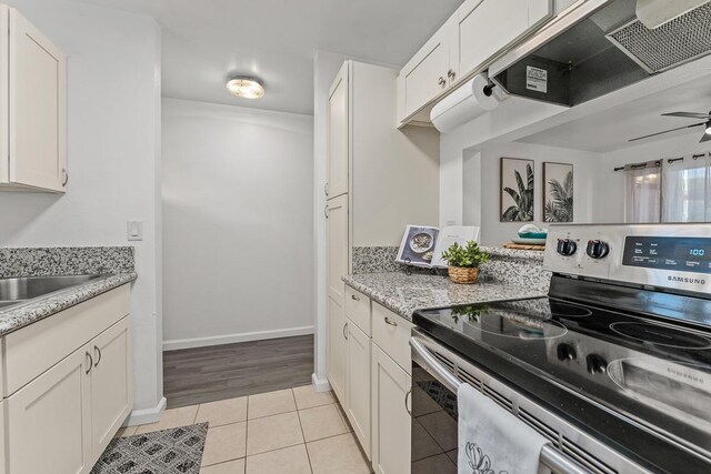 kitchen featuring electric stove, under cabinet range hood, light tile patterned flooring, white cabinets, and light stone countertops