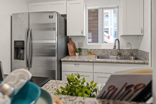kitchen with stainless steel fridge, a sink, white cabinetry, and light stone counters
