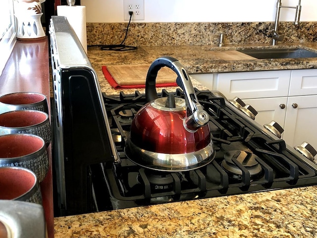 interior details with white cabinetry, sink, and dark stone countertops