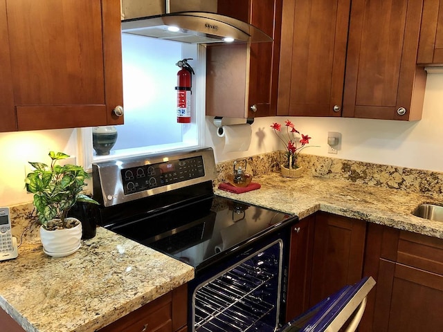 kitchen with light stone counters, sink, electric range, and exhaust hood