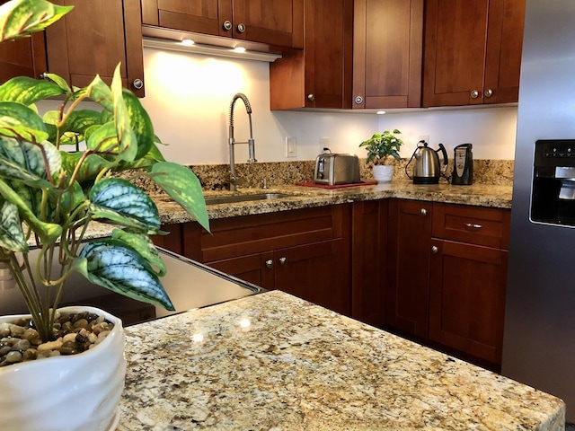 kitchen with light stone countertops, sink, stove, and stainless steel fridge with ice dispenser