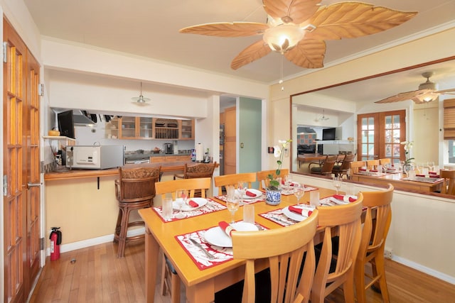 dining room with light wood-style flooring, a ceiling fan, baseboards, ornamental molding, and french doors