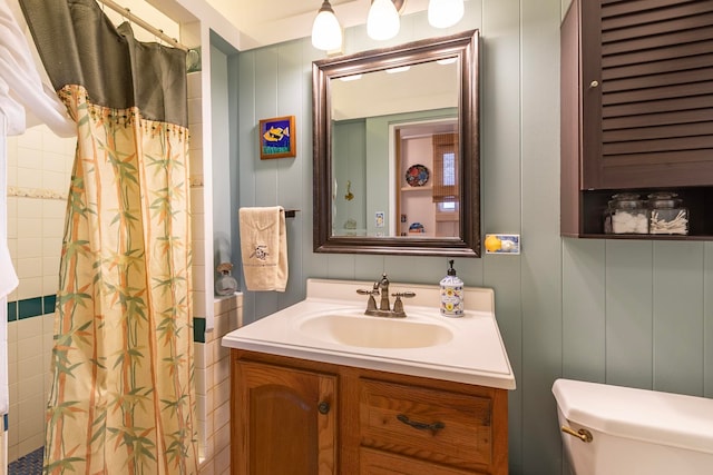 bathroom featuring a shower with shower curtain, vanity, toilet, and a decorative wall