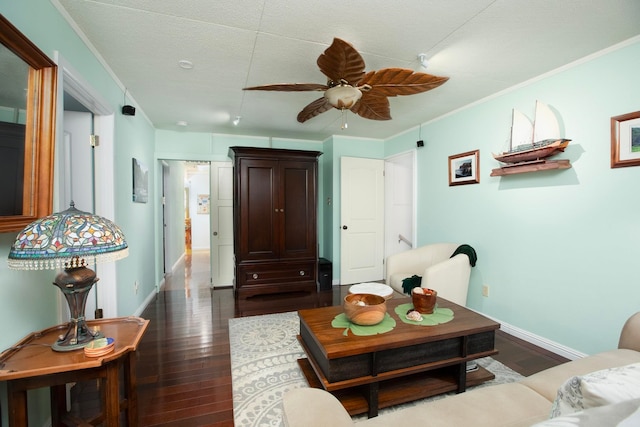 living room with ornamental molding, dark wood-style flooring, a ceiling fan, and baseboards