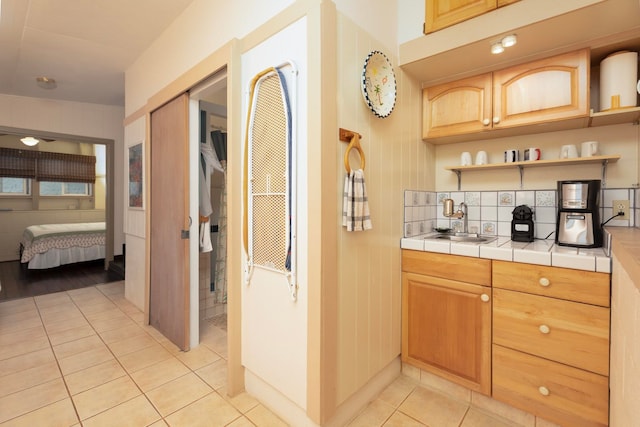 kitchen featuring tile countertops, light tile patterned floors, tasteful backsplash, open shelves, and a sink