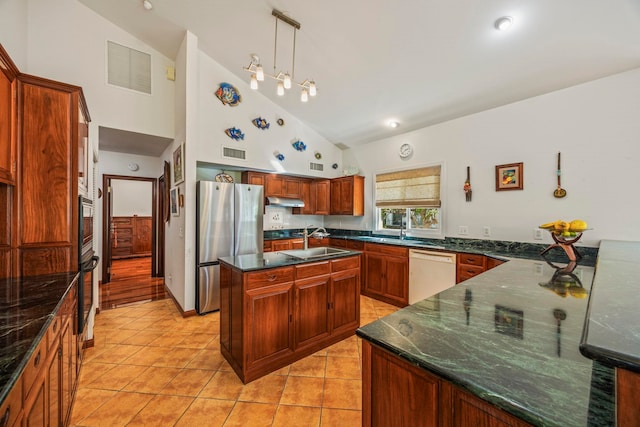 kitchen featuring high vaulted ceiling, white dishwasher, stainless steel fridge, an island with sink, and decorative light fixtures