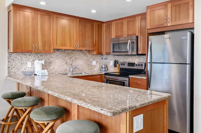 kitchen featuring appliances with stainless steel finishes, a breakfast bar, kitchen peninsula, decorative backsplash, and light stone countertops