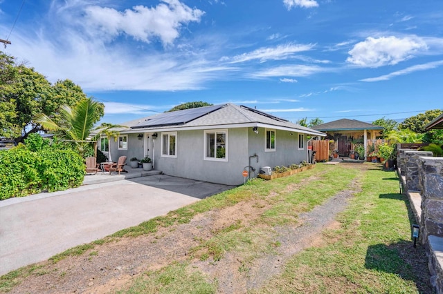 view of front of home featuring a front lawn, solar panels, and a patio area