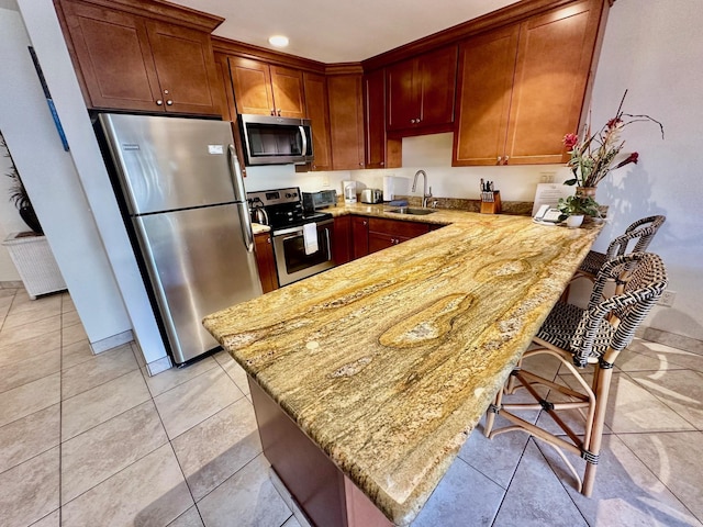 kitchen with sink, light stone countertops, appliances with stainless steel finishes, kitchen peninsula, and a breakfast bar area