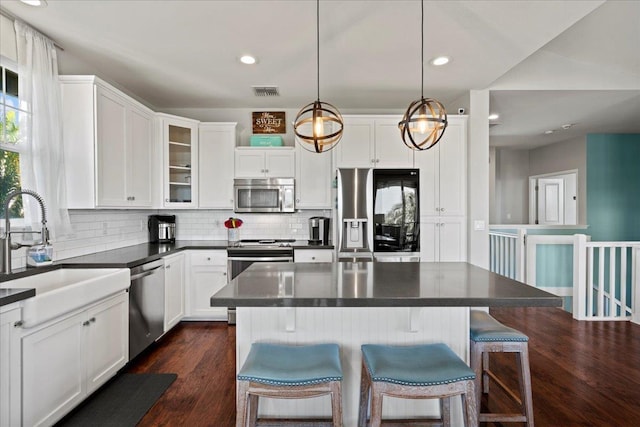 kitchen featuring decorative light fixtures, dark countertops, appliances with stainless steel finishes, glass insert cabinets, and white cabinetry