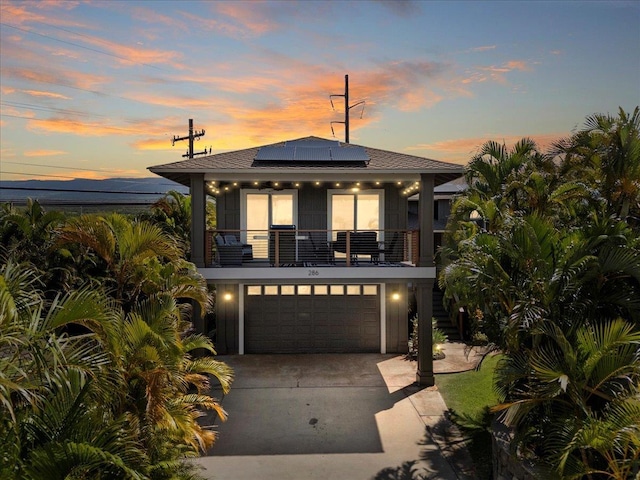 view of front facade featuring roof with shingles, solar panels, an attached garage, a balcony, and driveway