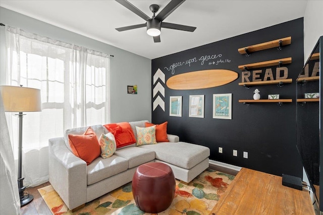 living room featuring an accent wall, light wood finished floors, a ceiling fan, and baseboards