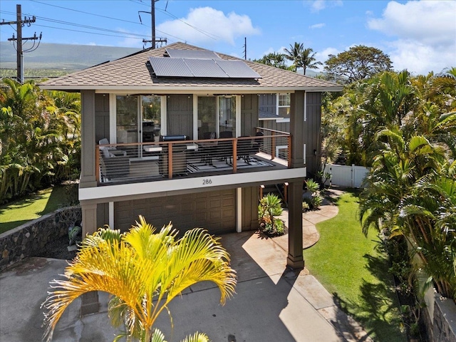 rear view of property with a yard, roof mounted solar panels, fence, a garage, and driveway