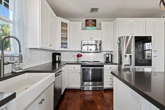 kitchen with appliances with stainless steel finishes, white cabinetry, glass insert cabinets, and visible vents