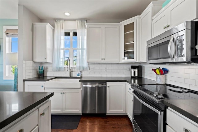 kitchen featuring appliances with stainless steel finishes, dark countertops, glass insert cabinets, and white cabinets