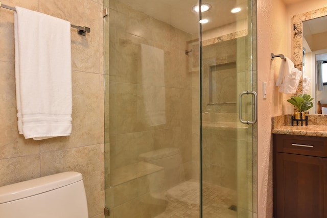 bathroom with tile walls, a shower with door, vanity, and toilet