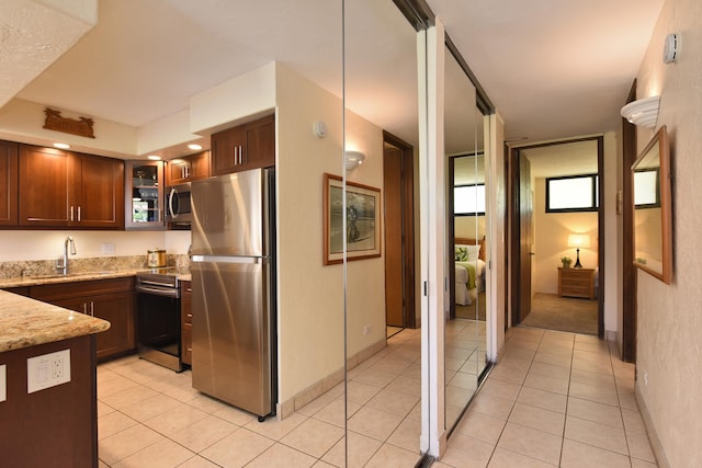 kitchen featuring appliances with stainless steel finishes, light tile floors, sink, and light stone countertops