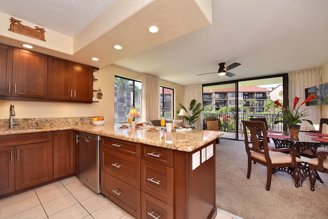 kitchen featuring light stone countertops, kitchen peninsula, ceiling fan, sink, and stainless steel dishwasher