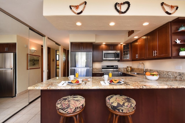 kitchen with kitchen peninsula, stainless steel appliances, light stone counters, sink, and light tile floors