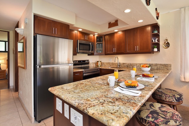 kitchen with light stone countertops, kitchen peninsula, stainless steel appliances, light tile floors, and sink