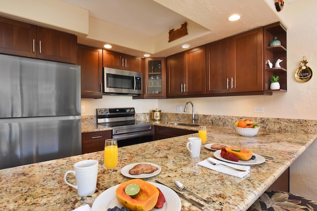 kitchen with sink, kitchen peninsula, stainless steel appliances, and light stone countertops