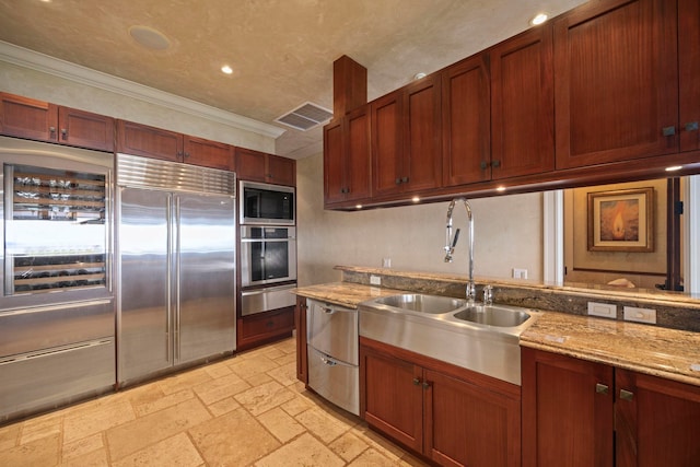 kitchen featuring light stone counters, built in appliances, light tile floors, sink, and ornamental molding