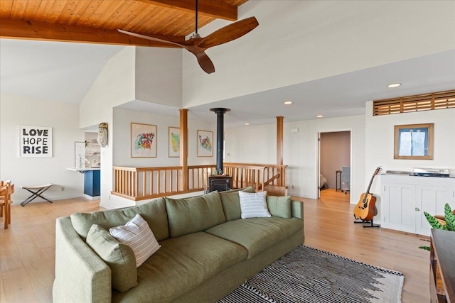 living room featuring beamed ceiling, wood ceiling, a wood stove, and light hardwood / wood-style flooring