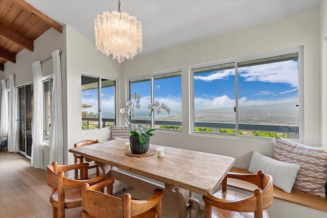 dining area featuring a wealth of natural light, a notable chandelier, vaulted ceiling with beams, and light hardwood / wood-style flooring