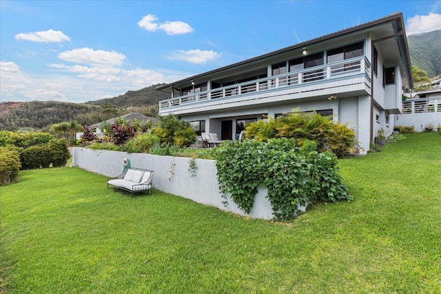 back of property with a mountain view, a balcony, and a yard