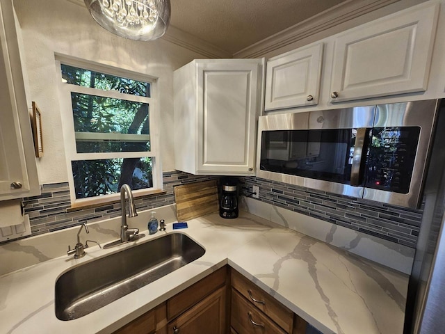 kitchen with light stone counters, tasteful backsplash, stainless steel microwave, white cabinetry, and a sink