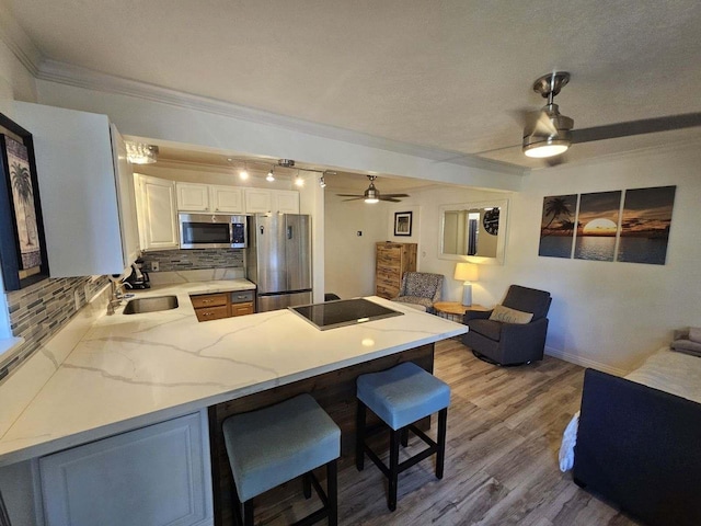 kitchen with stainless steel appliances, a breakfast bar, a peninsula, a sink, and a ceiling fan