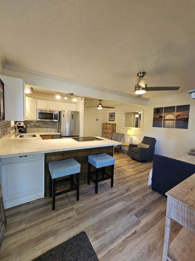 kitchen featuring a peninsula, a breakfast bar, a sink, appliances with stainless steel finishes, and backsplash