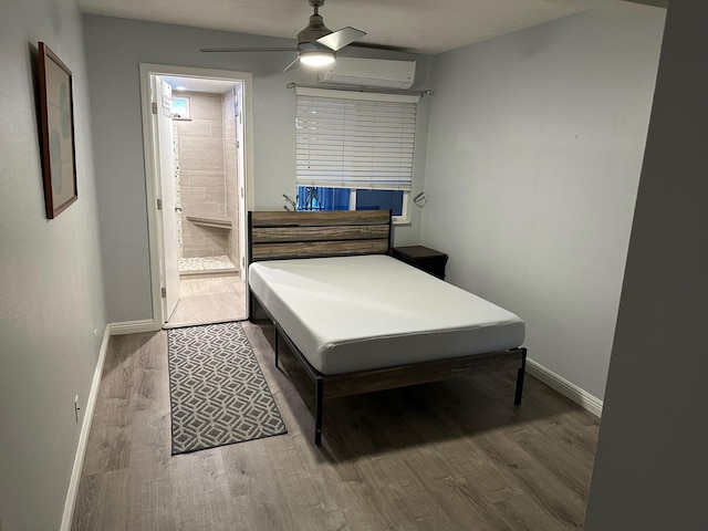 bedroom with ensuite bathroom, ceiling fan, wood finished floors, a wall mounted air conditioner, and baseboards