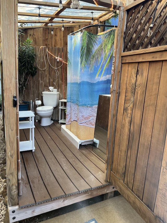 full bathroom with a shower with shower curtain, wood finished floors, toilet, and wooden walls