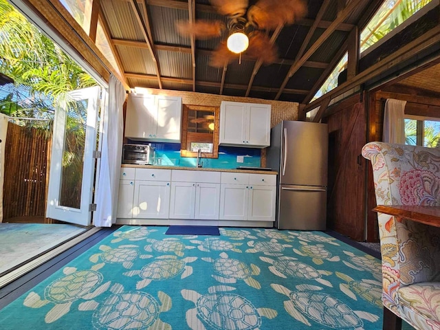 kitchen featuring freestanding refrigerator, white cabinets, a sink, and lofted ceiling