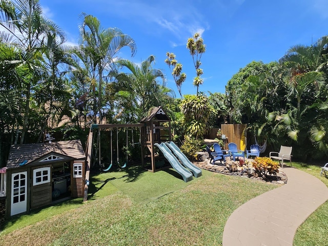 view of playground with an outdoor fire pit, fence, a lawn, and an outbuilding