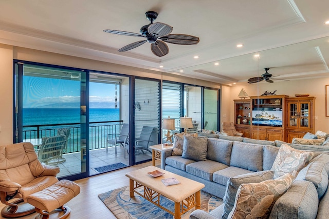 living room featuring ceiling fan, light wood-type flooring, ornamental molding, and a tray ceiling