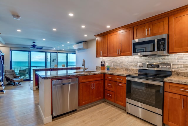 kitchen featuring a wall unit AC, kitchen peninsula, appliances with stainless steel finishes, and light hardwood / wood-style flooring