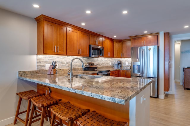 kitchen featuring sink, light stone counters, light hardwood / wood-style flooring, kitchen peninsula, and appliances with stainless steel finishes