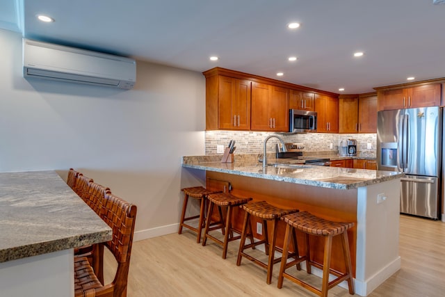 kitchen with kitchen peninsula, appliances with stainless steel finishes, tasteful backsplash, a wall mounted AC, and light hardwood / wood-style floors