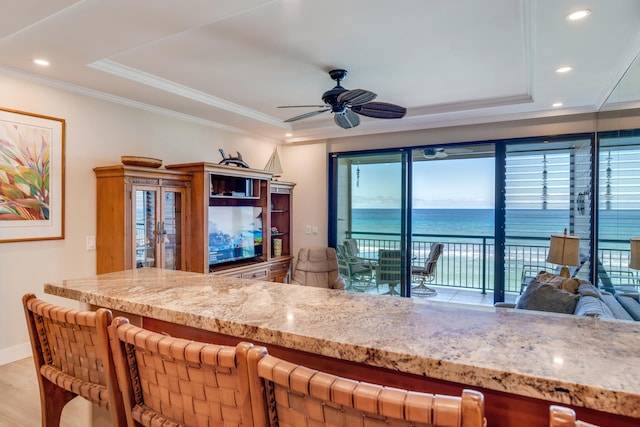 kitchen with light wood-type flooring, a tray ceiling, ceiling fan, and crown molding