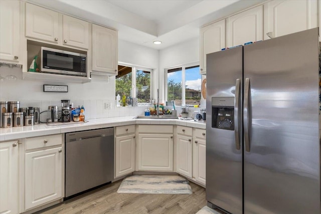 kitchen featuring white cabinets, backsplash, stainless steel appliances, tile countertops, and light hardwood / wood-style floors