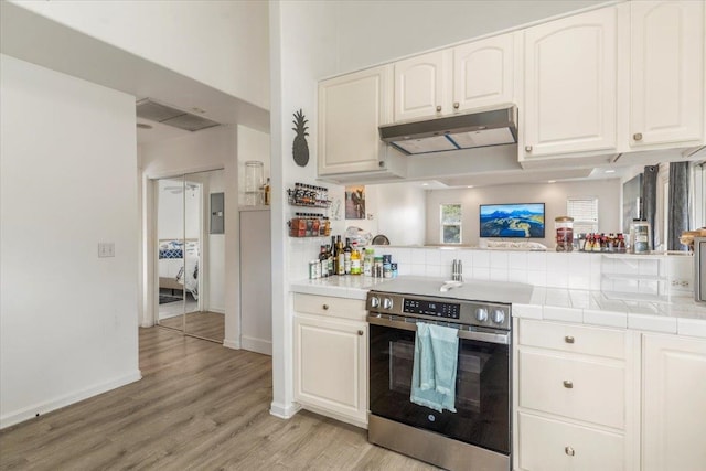 kitchen with white cabinets, kitchen peninsula, tile countertops, light wood-type flooring, and stainless steel range