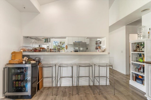 kitchen with a kitchen breakfast bar, white cabinets, light hardwood / wood-style floors, and stainless steel fridge