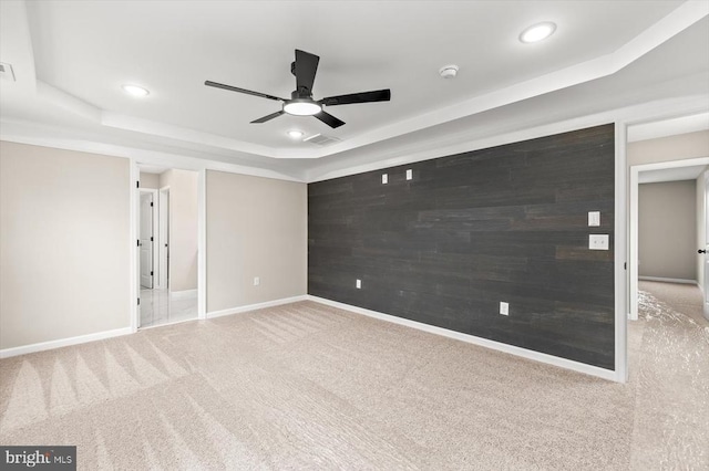 unfurnished room with carpet floors, a tray ceiling, an accent wall, wood walls, and baseboards