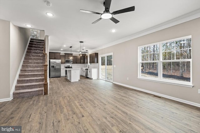 unfurnished living room featuring light wood finished floors, plenty of natural light, stairway, and ornamental molding